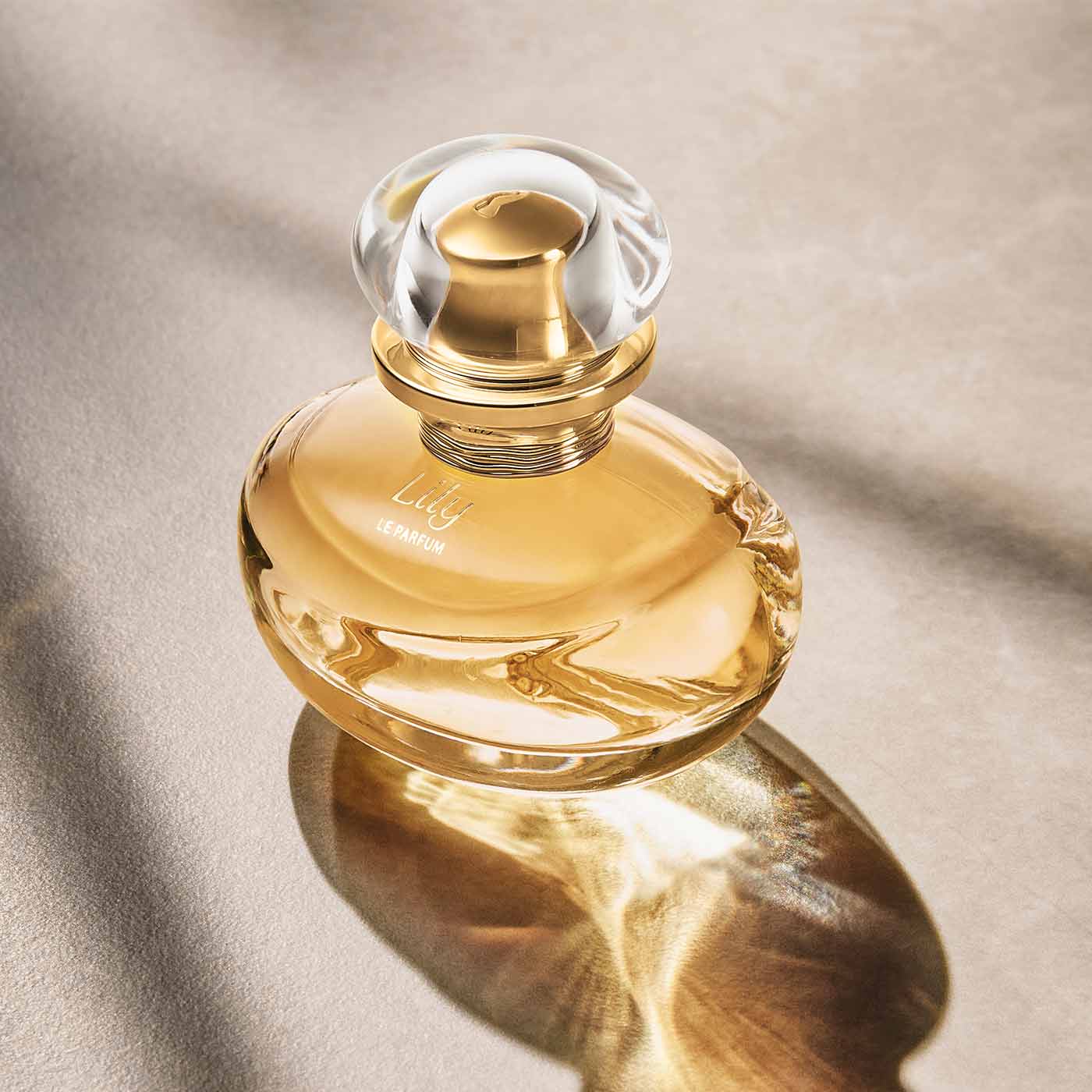 Este é um frasco do perfume Lily Le Parfum da marca Boticário. A embalagem é em vidro transparente, com um líquido amarelo claro dentro e uma tampa dourada. O rótulo tem o nome do perfume em letras elegantes e a marca O Boticário em destaque.